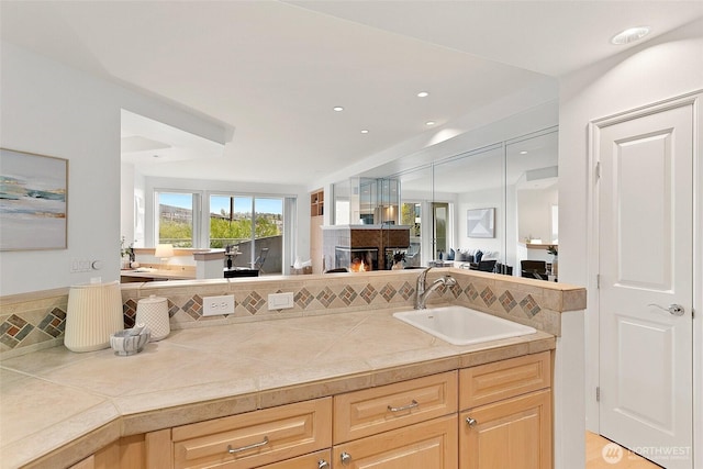 3900 2nd Ave NE Unit 204, Seattle, WA 98105 - kitchen featuring a sink, open floor plan, light brown cabinets, a multi sided fireplace, and light countertops