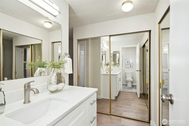 12721 NE 116th St Unit F102, Kirkland, WA 98034 - bathroom with vanity, wood finished floors, toilet, and a textured ceiling