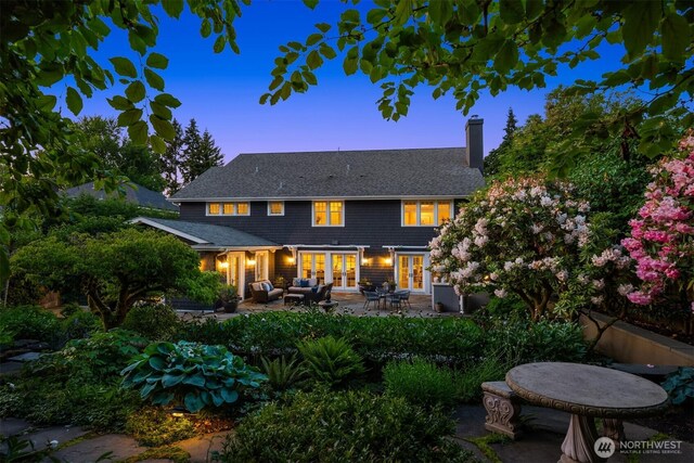 1325 Broadmoor Dr E, Seattle, WA 98112 - back of property at dusk with french doors, a chimney, a patio area, an outdoor hangout area, and a shingled roof
