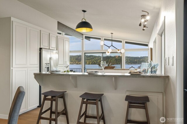 5110 NW Sammamish Rd, Issaquah, WA 98027 - kitchen featuring stainless steel refrigerator with ice dispenser, a kitchen bar, hanging light fixtures, a water view, and white cabinetry
