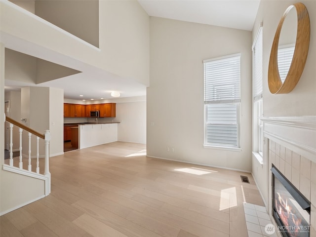 23501 112th Ave SE Unit M104, Kent, WA 98031 - unfurnished living room featuring light wood-style floors, a tiled fireplace, baseboards, stairway, and high vaulted ceiling
