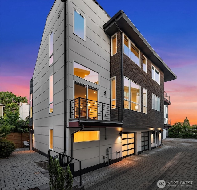 818 25th Ave S Unit A, Seattle, WA 98144 - back of house at dusk featuring a garage, a balcony, and driveway