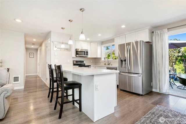 1980 Mckinley St, Enumclaw, WA 98022 - kitchen with stainless steel appliances, a breakfast bar, white cabinetry, wood finished floors, and light countertops