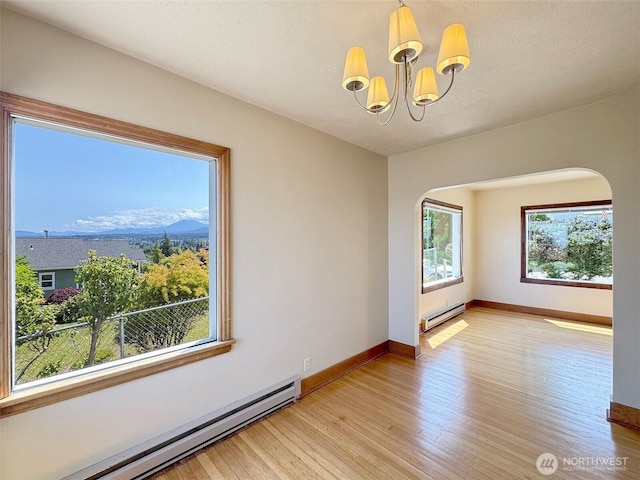 1025 W 6th St, Port Angeles, WA 98363 - empty room with a baseboard heating unit, arched walkways, light wood-style flooring, and a chandelier