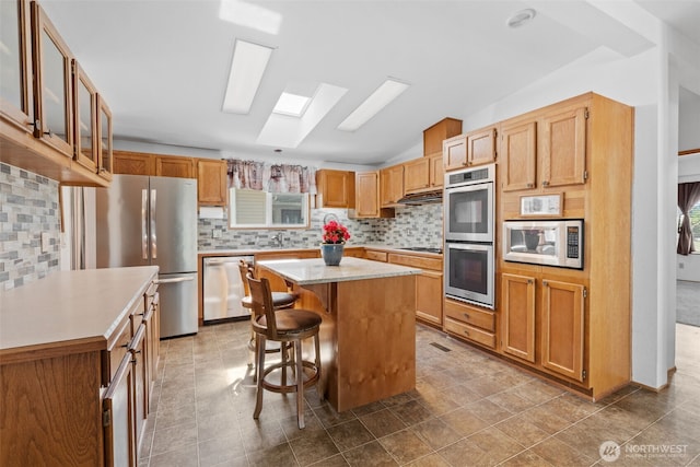 1402 22nd St NE Unit 438, Auburn, WA 98002 - kitchen featuring stainless steel appliances, vaulted ceiling, backsplash, a breakfast bar area, and light countertops