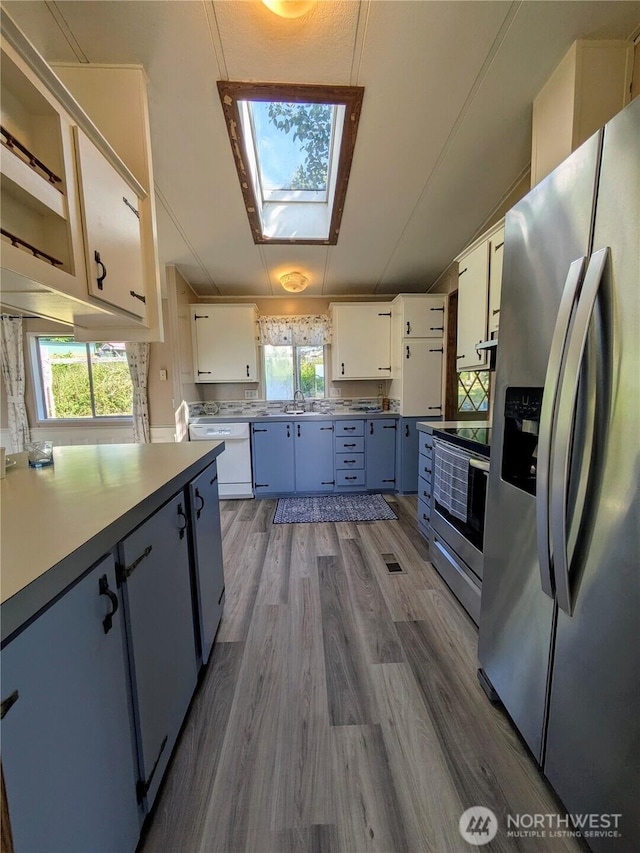 201 Hemlock St, Orcas Island, WA 98245 - kitchen featuring stainless steel appliances, a skylight, wood finished floors, white cabinetry, and a sink