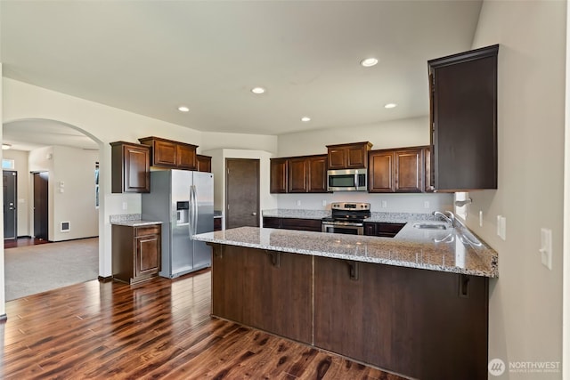 2212 N Creeksedge Way, Ellensburg, WA 98926 - kitchen featuring appliances with stainless steel finishes, a peninsula, arched walkways, dark wood-style flooring, and light stone counters