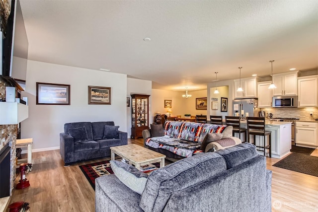 12911 NE 61st Ave, Vancouver, WA 98686 - living room with light wood-style floors, a stone fireplace, baseboards, and a chandelier
