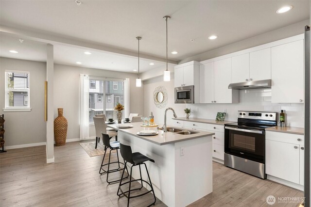 3123 148th St SW Unit A6, Lynnwood, WA 98087 - kitchen featuring appliances with stainless steel finishes, under cabinet range hood, a sink, a kitchen bar, and light wood-style floors