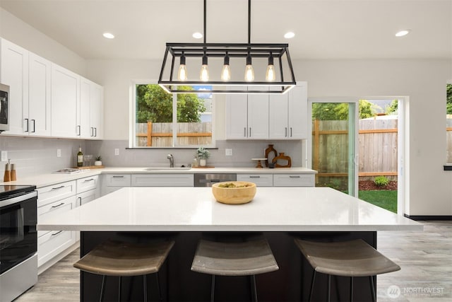 9245 Kelsey Ln SW, Seattle, WA 98106 - kitchen with stainless steel appliances, a breakfast bar, light countertops, light wood finished floors, and decorative backsplash