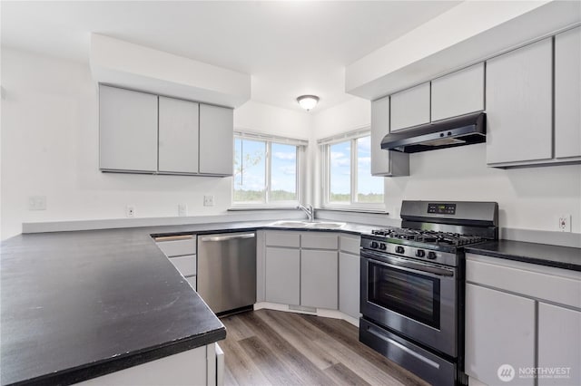 1258 NW Timber Shadow Ct, Silverdale, WA 98380 - kitchen featuring appliances with stainless steel finishes, under cabinet range hood, a sink, wood finished floors, and dark countertops