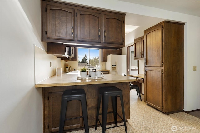 18801 86th Pl W, Edmonds, WA 98026 - kitchen featuring white fridge with ice dispenser, a peninsula, light countertops, a kitchen bar, and dark brown cabinets