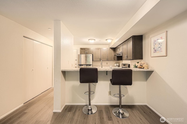 3022 SW Bradford St Unit 205, Seattle, WA 98126 - kitchen with freestanding refrigerator, stove, dark wood-style floors, light countertops, and a breakfast bar