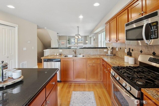7121 Shinkle Pl SW, Seattle, WA 98106 - kitchen featuring stainless steel appliances, a sink, a peninsula, light wood finished floors, and brown cabinets
