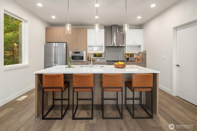 4576 22nd Ave SW, Seattle, WA 98106 - kitchen with wall chimney range hood, appliances with stainless steel finishes, decorative backsplash, dark wood-type flooring, and a center island with sink
