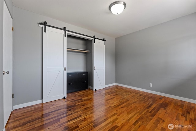 1115 S Evergreen Dr, Moses Lake, WA 98837 - unfurnished bedroom with a barn door, wood finished floors, and baseboards