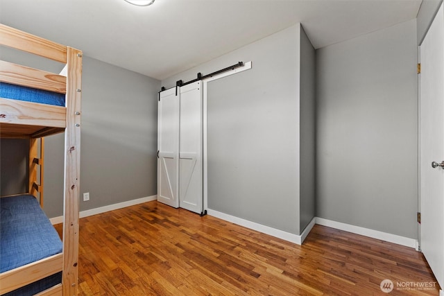 1115 S Evergreen Dr, Moses Lake, WA 98837 - unfurnished bedroom featuring a barn door, wood finished floors, and baseboards