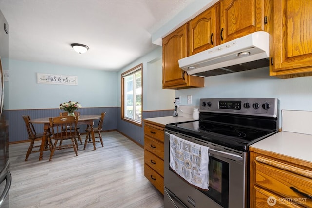23696 Lake Dr, Mount Vernon, WA 98273 - kitchen featuring stainless steel electric range oven, under cabinet range hood, brown cabinetry, light countertops, and a wainscoted wall