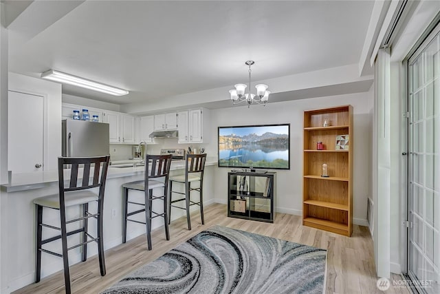 3939 10th St SE Unit A2, Puyallup, WA 98374 - kitchen with light wood-style flooring, under cabinet range hood, a chandelier, white cabinetry, and stainless steel appliances
