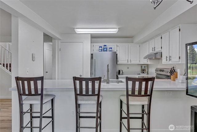 3939 10th St SE Unit A2, Puyallup, WA 98374 - kitchen featuring under cabinet range hood, appliances with stainless steel finishes, light countertops, white cabinets, and a peninsula