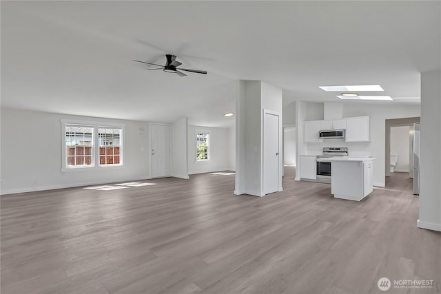7725 203rd Street Ct E Unit 27, Spanaway, WA 98387 - unfurnished living room with lofted ceiling, light wood finished floors, a skylight, baseboards, and ceiling fan