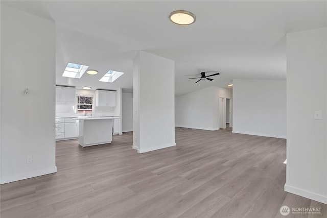 7725 203rd Street Ct E Unit 27, Spanaway, WA 98387 - unfurnished living room featuring a skylight, light wood-style flooring, baseboards, lofted ceiling, and ceiling fan