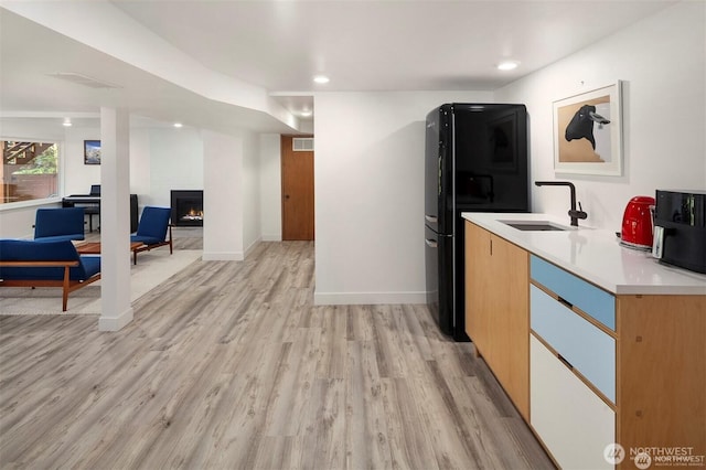 10762 Exeter Ave NE, Seattle, WA 98125 - kitchen with a sink, freestanding refrigerator, a lit fireplace, light wood-style floors, and light countertops