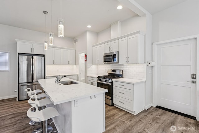 7724 16th Ave SW, Seattle, WA 98106 - kitchen with appliances with stainless steel finishes, a sink, white cabinets, a kitchen bar, and recessed lighting