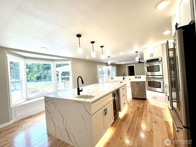 4012 267th St E, Spanaway, WA 98387 - kitchen featuring appliances with stainless steel finishes, a sink, light wood-type flooring, a kitchen island with sink, and white cabinetry