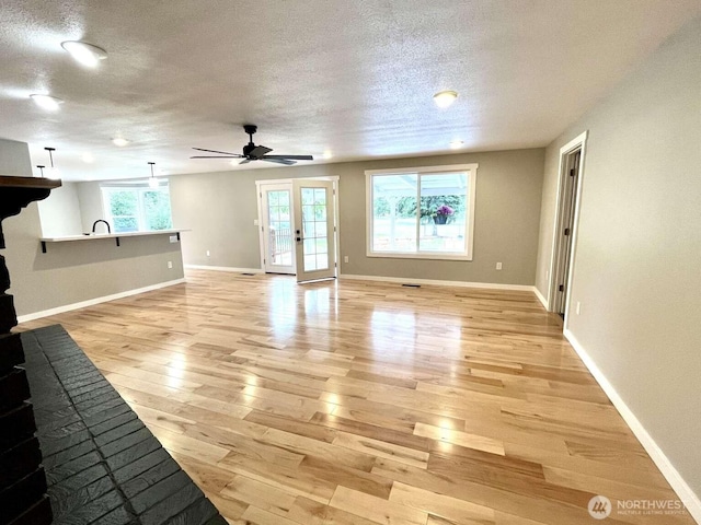 4012 267th St E, Spanaway, WA 98387 - unfurnished living room with light wood-type flooring, a textured ceiling, baseboards, a ceiling fan, and a sink