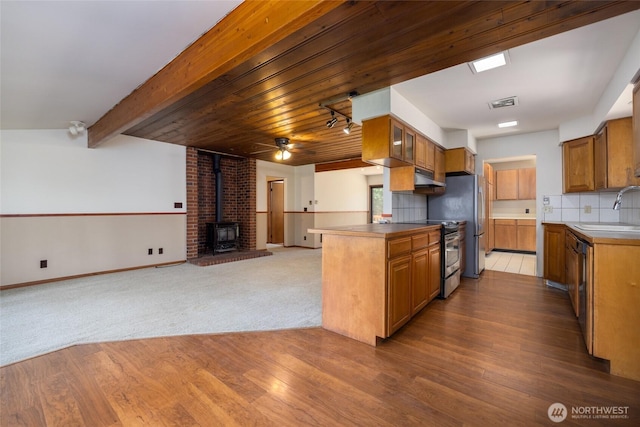 16757 Chilberg Ave, La Conner, WA 98257 - kitchen featuring appliances with stainless steel finishes, a wood stove, under cabinet range hood, brown cabinets, and open floor plan