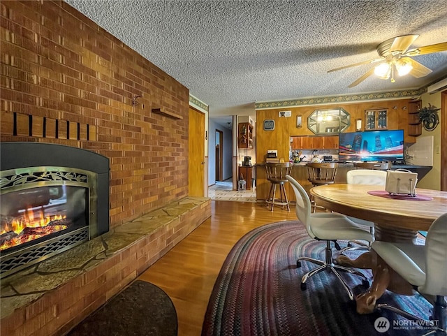 2208 Sandra Ave, Centralia, WA 98531 - dining room featuring a textured ceiling, wood finished floors, brick wall, a fireplace, and a ceiling fan
