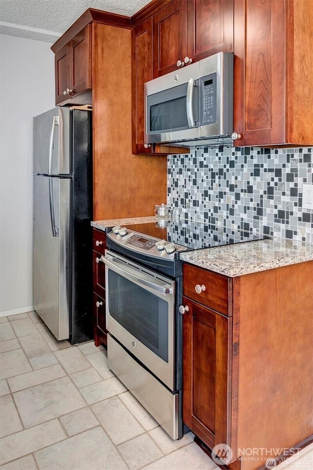 4561 Lake Washington Blvd NE Unit 303, Kirkland, WA 98033 - kitchen with stainless steel appliances, backsplash, light stone countertops, baseboards, and a textured ceiling