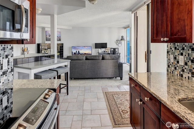 4561 Lake Washington Blvd NE Unit 303, Kirkland, WA 98033 - kitchen featuring appliances with stainless steel finishes, tasteful backsplash, light stone countertops, reddish brown cabinets, and a textured ceiling