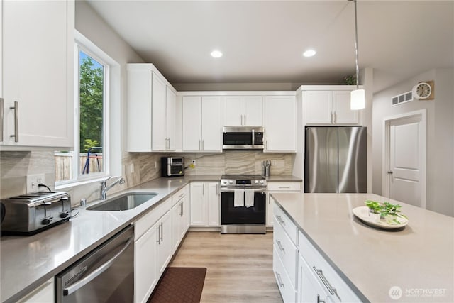 4305 23rd Ct NE, Olympia, WA 98516 - kitchen featuring appliances with stainless steel finishes, a sink, white cabinetry, backsplash, and light wood-style flooring