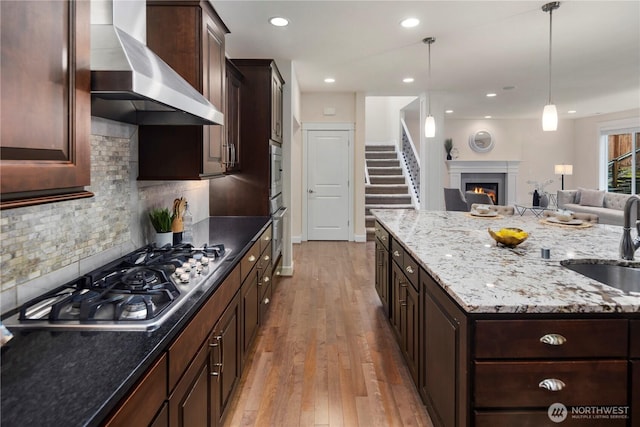 24332 NE 8th Pl, Sammamish, WA 98074 - kitchen with wall chimney range hood, appliances with stainless steel finishes, a sink, open floor plan, and light wood-style flooring