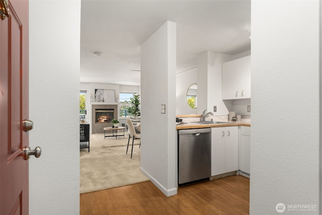 2244 13th Ave W Unit 106, Seattle, WA 98119 - kitchen with dishwasher, light wood-style flooring, white cabinets, a tile fireplace, and light countertops