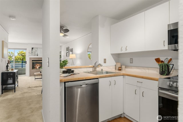 2244 13th Ave W Unit 106, Seattle, WA 98119 - kitchen featuring appliances with stainless steel finishes, light carpet, white cabinets, a tile fireplace, and a peninsula