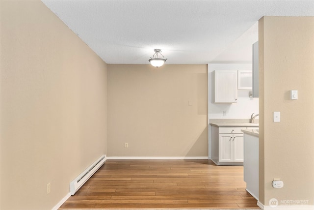 750 N 143rd St Unit 211, Seattle, WA 98133 - unfurnished dining area with a baseboard heating unit, light wood finished floors, a sink, and baseboards