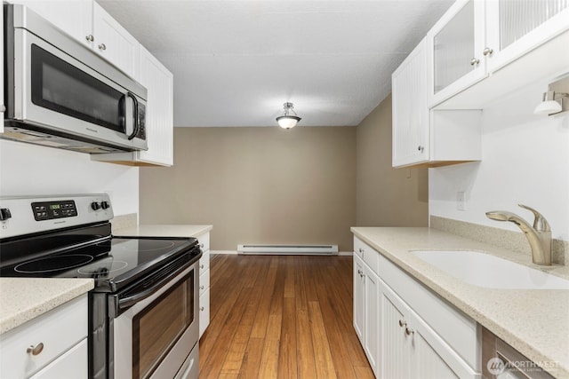 750 N 143rd St Unit 211, Seattle, WA 98133 - kitchen featuring appliances with stainless steel finishes, a sink, baseboard heating, and white cabinetry