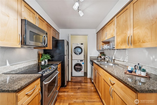 3045 20th Ave W Unit 107, Seattle, WA 98199 - kitchen with stainless steel appliances, stacked washer / drying machine, a sink, wood finished floors, and dark stone countertops