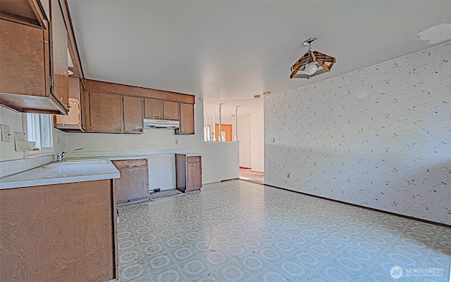24427 14th Ave S, Des Moines, WA 98198 - kitchen with under cabinet range hood, a sink, light flooring, wallpapered walls, and light countertops