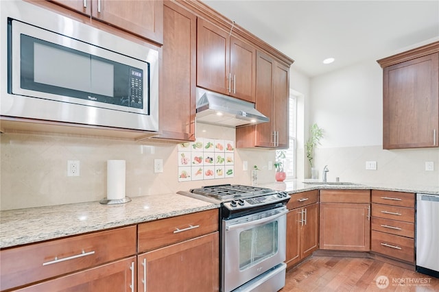 10821 Eastridge Dr NE, Redmond, WA 98053 - kitchen with stainless steel appliances, a sink, under cabinet range hood, light wood-style flooring, and backsplash