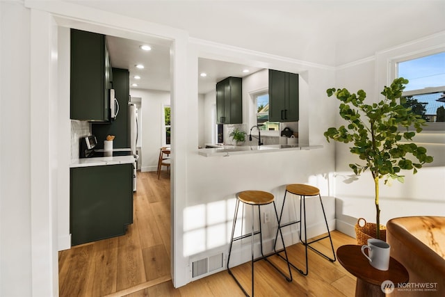 3722 36th Ave SW, Seattle, WA 98126 - kitchen with green cabinetry, light countertops, a kitchen bar, light wood-type flooring, and recessed lighting