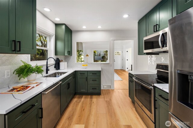 3722 36th Ave SW, Seattle, WA 98126 - kitchen featuring green cabinets, appliances with stainless steel finishes, a sink, light wood-type flooring, and backsplash