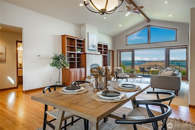 8022 Makah Rd, Blaine, WA 98230 - dining room with beam ceiling, light wood-style flooring, a tiled fireplace, a ceiling fan, and high vaulted ceiling