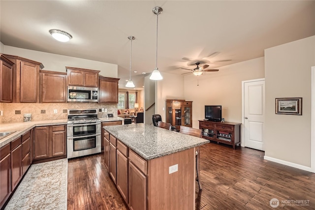 4306 Maple St SE, Olympia, WA 98501 - kitchen with appliances with stainless steel finishes, decorative backsplash, dark wood-style flooring, a center island, and a breakfast bar
