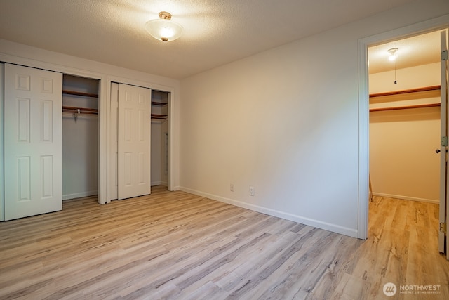 4456 Whitman Ave N, Seattle, WA 98103 - unfurnished bedroom with light wood-style floors, baseboards, multiple closets, and a textured ceiling