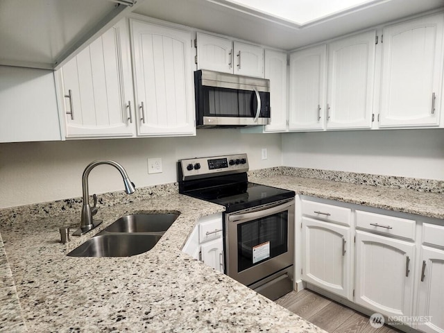 2611 NE 4th St Unit 234, Renton, WA 98056 - kitchen with stainless steel appliances, a sink, white cabinets, light wood-type flooring, and light stone countertops