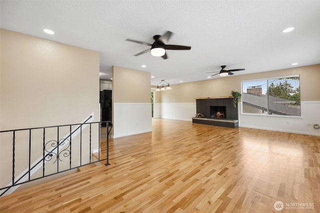 104 Hawthorn Ln, Shelton, WA 98584 - unfurnished living room with ceiling fan, wainscoting, light wood-style flooring, a lit fireplace, and recessed lighting